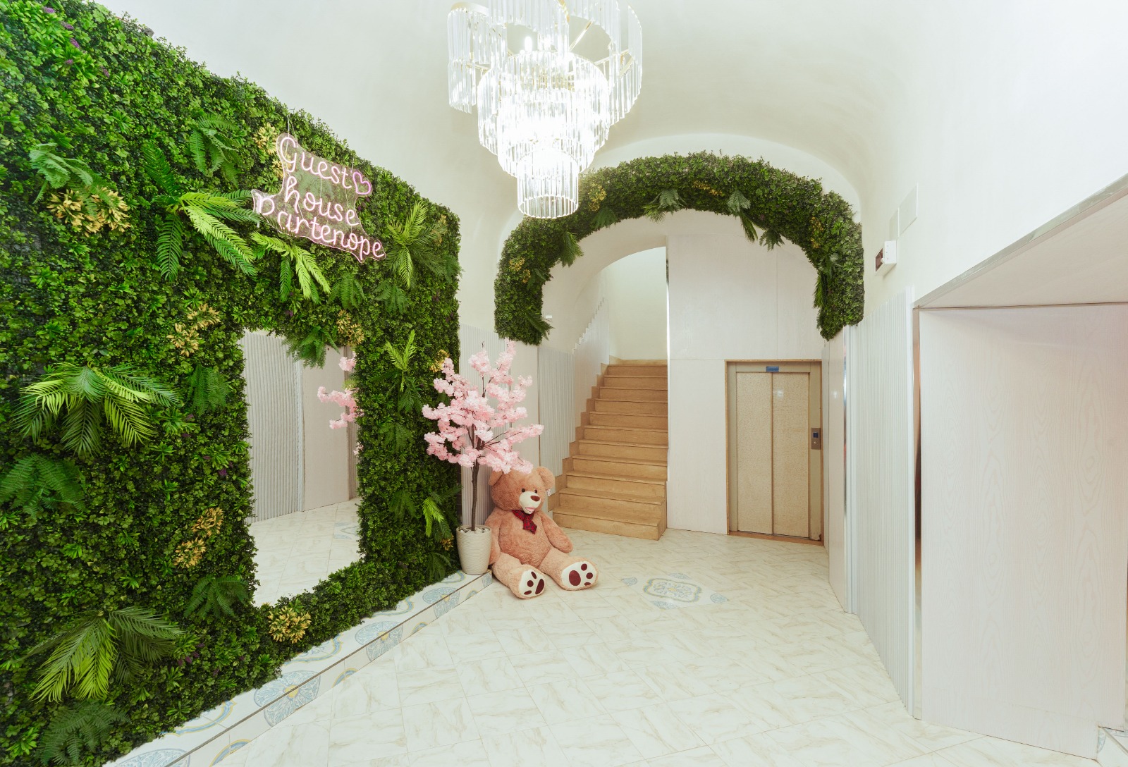 The image depicts a luxurious hallway featuring a large green wall with a neon sign, a chandelier, and an elevator. * **La...